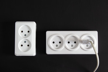 Two white sockets on a black background into one of which a plug is stuck.
