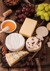 Selection of various cheese on the board and grapes on wooden background. Blue Stilton, Red Leicester and Brie Cheese and bowl of nuts with honey. Top view.