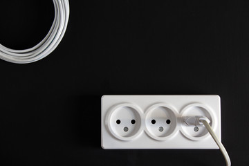 White socket with a stuck plug on a dark background with a wire lying next to it.