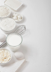 Fototapeta na wymiar Fresh dairy products on white table background. Glass of milk, bowl of flour, sour cream and cottage cheese and eggs. Steel whisk. Top view