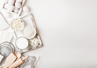 Fresh dairy products on white table background. Glass of milk, bowl of flour and cottage cheese and eggs. Box of baking utensils. whisk and spatula in vintage wooden box.Top view. Space for text
