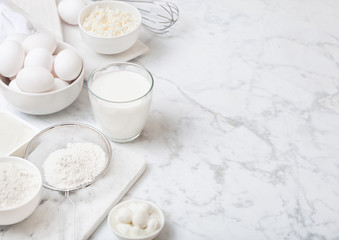 Fresh dairy products on white marble background. Glass of milk, bowl of flour, sour cream and cottage cheese and eggs. Steel whisk. Top view. Space for text