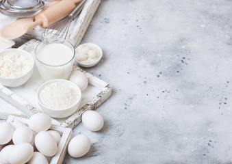 Fresh dairy products on white table background. Glass of milk, bowl of flour and cottage cheese and eggs. Box of baking utensils. whisk and spatula in vintage wooden box.Top view. Space for text