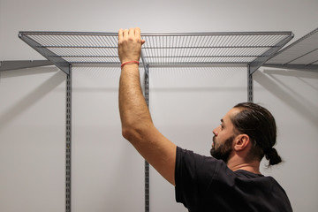A working fitter man with a beard mounts metal racks on the wall.