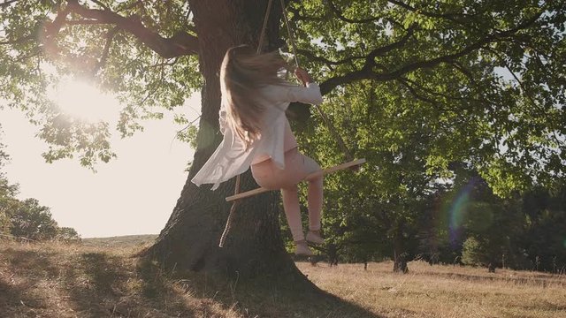 Girl enjoy summer on a rope swing spinning with hair flowing - low angle, camera slowly descend