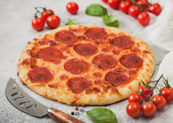 Fresh round baked Pepperoni italian pizza with knife with tomatoes and basil on light background with linen towel.