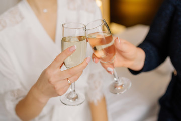 Gorgeous bride and bridesmaid toasting champagne and having fun on wedding morning. Cheerful young girlfriends raise a toast and clink glasses. Bride morning. Wedding day