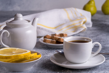 Cup of tea, teapot, cakes and lemon on a table, pears on blurred bokeh background.