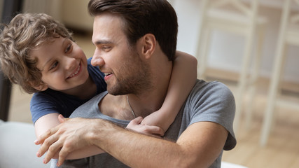 Fototapeta premium Close up of smiling small preschooler boy child piggyback embrace happy young dad having fun at home together, loving father and little son hug cuddle enjoy free time leisure weekend indoors