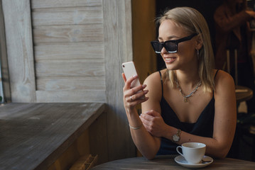 Fashionable girl in sunglasses in a cafe sits in the phone with a cup of coffee. copy space.