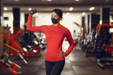 Coronavirus covid-19 prevention, fitness girl with a medical mask holding a dumbbell . Fighting...