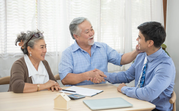 Smiling Satisfied Senior Couple Making Sale Purchase Deal Concluding Contract From Real Estate Agent,happy Older Family And Broker Shake Hands Agreeing To Buy New House At Meeting.