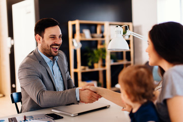 Single mother with a small child in her lap shakes hands with manager in the bank