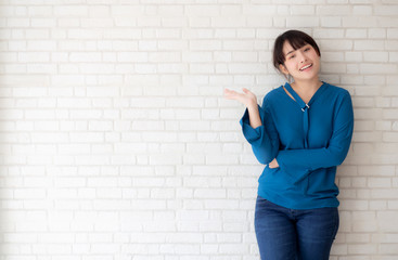 Beautiful young asian woman standing and smiling happy and presenting something and showing future or planning with message of you on cement concrete background, lifestyle concept.
