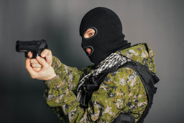 A man in camouflage uniform, body armor and a balaclava, holds his weapon ready and takes aim with...
