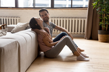 Overjoyed young couple sit on warm wooden floor in cozy renovated apartment laugh having fun, happy...