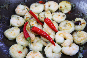 Closeup of isolated fried spicy fresh tiger shrimps in wok pan with shiny red chillies