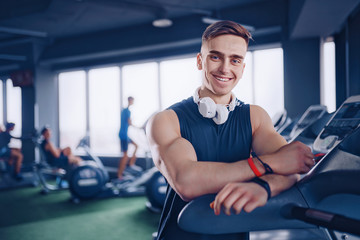 Smiling positive confident male personal instructor with arms crossed arms near treadmill at gym in fitness gym.