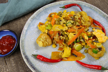 Closeup of isolated china plate with spicy fresh thai fried rice food, carrots, peas, shrimps, chicken, Chillies, maize, eggs seasoned with turmeric on wood table prepared in wok pan