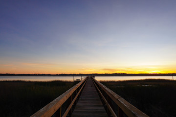 A long dock leads out to a marsh and river at sunset in South Carolina; copy space