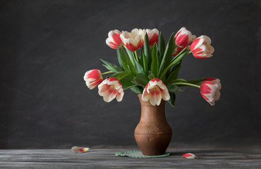Still life. Tulips Bouquet in a clay jug on a wooden table. Rustic style. © symbol344
