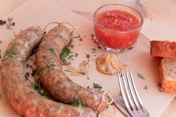 Homemade sausages on paper with mustard and tomato sauce. Cutlery and bread. Top view on a wooden background. Hands holding cutlery.