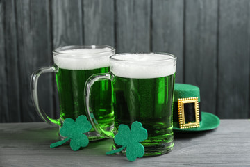 Green beer, hat and clover leaves on grey wooden table. St. Patrick's Day celebration