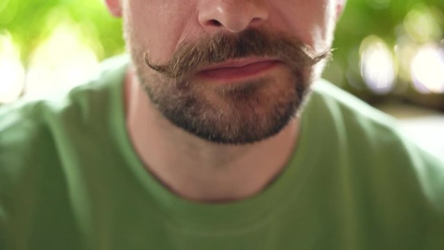 Bearded man with curled up mustache eats chocolate eclair in cafe