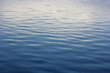 a soothing background with blue water of the river with small ripples and the reflected clouds