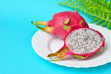 Close up view of exotic dragon fruit cut and whole sliced isolated on a blue background with leafs.
