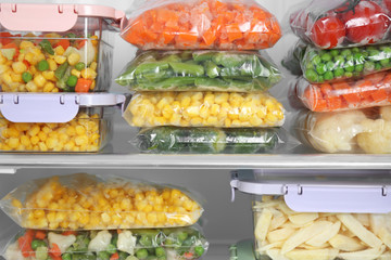 Plastic bags and containers with different frozen vegetables in refrigerator