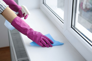 Woman cleaning window sill with rag and detergent indoors, closeup