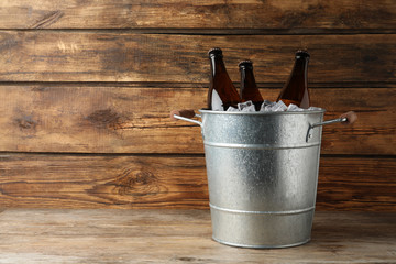 Metal bucket with beer and ice cubes on wooden background. Space for text