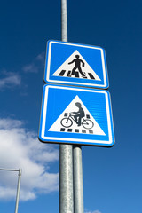 Traffic sign on the road - pedestrian crossing, crosswalk and crossing for biker and cyclist on bike and bicycle on the cycle path. Blue sky in the background.