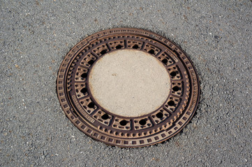 Manhole and utility hole in the asphalt surface. Rounded cover made of steel and metal is rusty.