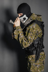 A man in a balaclava with a skull pattern, dressed in camouflage with a hood and a bulletproof...