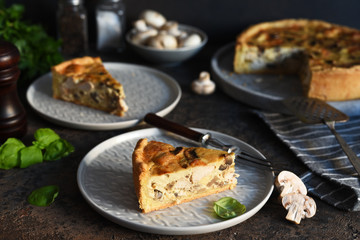 Tart slice on the kitchen table. Traditional quiche with chicken, mushrooms and cheese on a dark concrete background.