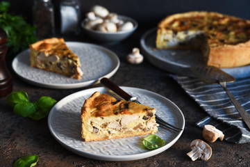 Tart slice on the kitchen table. Traditional quiche with chicken, mushrooms and cheese on a dark concrete background.