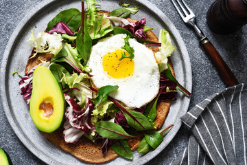 Classic breakfast - fried eggs, salad with avocado and bread toast on a concrete background.