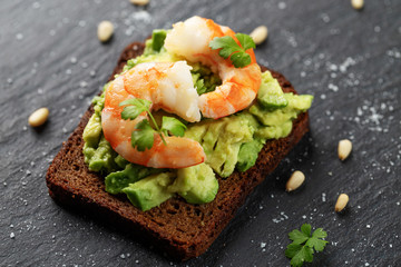 Toast with shrimp, avocado, nuts, parsley on dark background
