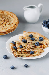 Thin pancakes on white plate with blueberries and sour cream. Grey background. Close up.