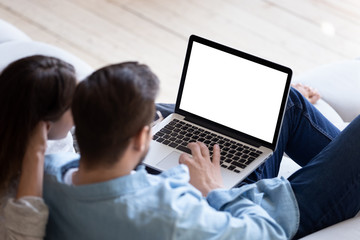 Loving couple looking at laptop screen blank white mockup close up, sitting on cozy sofa, young man...