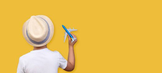 The back of a boy in a hat holding a plane in his hands on a yellow background. Copy space. Summer vacation concept.