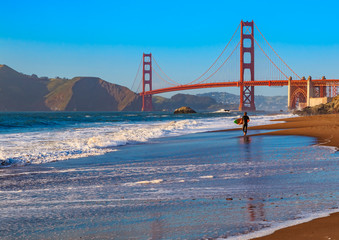 Unidentified surfer at sunset at Baker Beach by the famous Golden Gate Bridge, San Francisco, California, USA