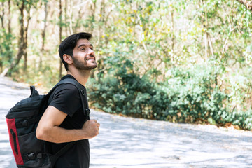 Closeup of cheerful young caucasian man in black t-shirt with backpack standing and looking to forest at National Park. Trekking and hiking travel concent.