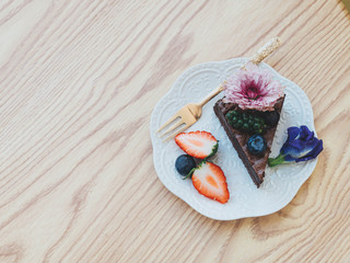 Top view.Chocolate brownie cake decorated with strawberries and blueberries, purple flowers and pepper on a wooden table