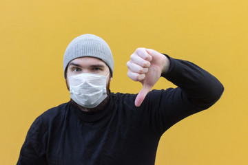 a man in a black jacket wearing a disposable mask to protect against coronavirus. Yellow background, emotions on the face. Person in a grey hat. Safety measures in case of illness.