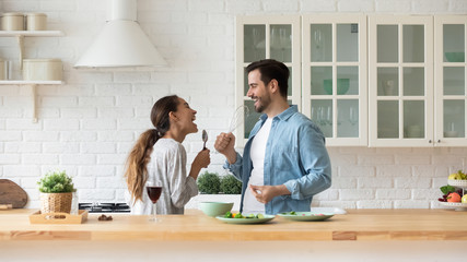 Happy loving couple singing song and dancing, having fun with kitchenware in kitchen, funny excited...