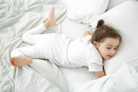 A cute little girl is sleeping in a white bed .