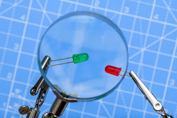 Close-up of red and green led electrical components held by crocodile-clips and seen through magnifying glass on blue background. Concept of electronics, science, industry, hobby or education.